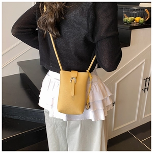 Detail view of yellow leather phone bucket bag with silver metal buckle on a model