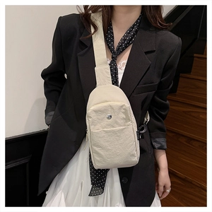 Detail of a minimalist beige nylon chest bag with zip pockets and black shoulder strap