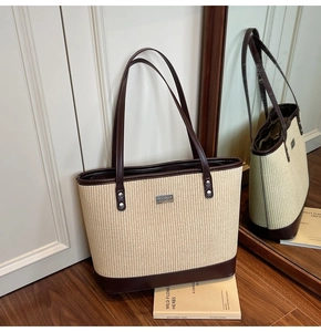 Detail view of woven straw tote bag with brown leather trim and silver logo plaque