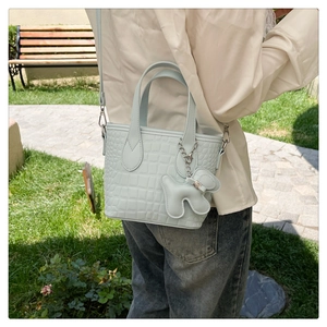 Pale blue crocodile pattern bucket bag with cute puppy charm shown in outdoor park setting