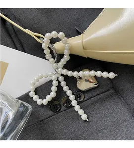 Detail of pearl bow charm and silver heart pendant on a stylish cream dumpling bag