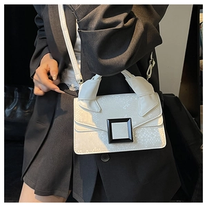 Detailed view of white snake-embossed leather handbag with black metal buckle and strap