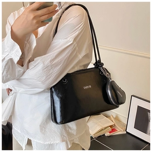 Détail d'un sac seau en cuir noir brillant avec pendentif porte-monnaie et fines bandoulières
