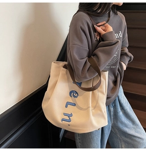 Detail of cream canvas tote bag with blue eln. embroidery and brown durable shoulder straps
