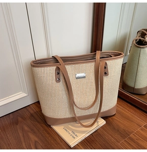 Detail of woven straw tote bag featuring brown leather trim and metallic brand plaque