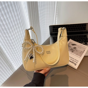 Detail of cream yellow leather shoulder bag with pearl bow charm and silver zipper