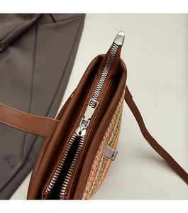 Detail of silver zipper closure on rainbow woven beach bag with brown leather trim