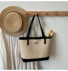 Detail of woven straw tote bag with black leather base and handles against summer attire