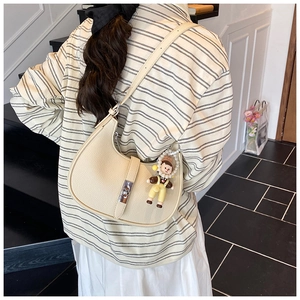 Detail of beige hobo bag with pebble leather texture and cute doll charm on shoulder strap
