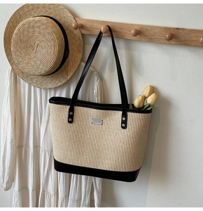 Close-up of beige woven tote bag with black leather straps and silver logo detail