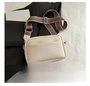 Close-up of beige lychee leather crossbody bag with striped strap and phone for scale