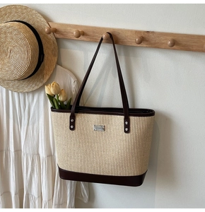 Detail of woven straw tote bag with brown leather trim and metal logo on wood hanger
