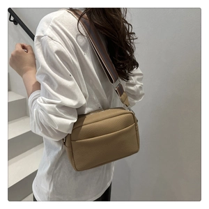 Detail view of light brown litchi pattern crossbody bag with a striped woven strap