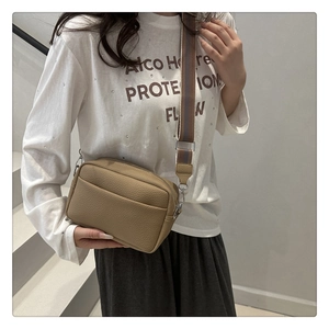Close-up of litchi textured khaki crossbody bag with wide striped shoulder strap