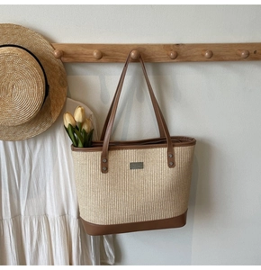 Detail of hand-woven straw tote bag with brown leather trim and metal logo plate