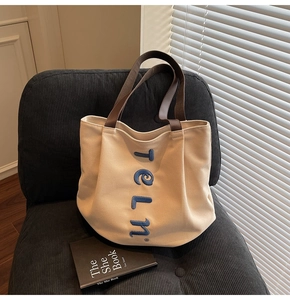 Detailed view of blue embroidered letters on beige canvas tote bag with brown straps