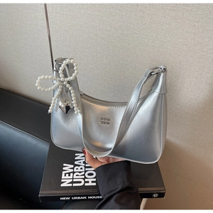 Detailed view of silver crescent bag with pearl bow charm and heart pendant on books