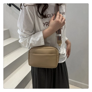 Close-up of light brown litchi pattern leather crossbody bag with wide striped strap