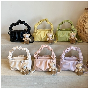 Close-up of ruched shoulder bags in six colors with bear charms on stone steps