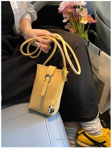 Detail of yellow lychee grain leather phone bag with silver horseshoe buckle and heart charm
