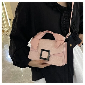 Pink crossbody bag with large bow handle and black square buckle detail on black outfit