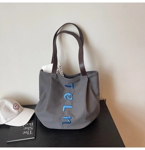 Detail of grey canvas tote bag featuring blue vertical embroidery and brown leather handles