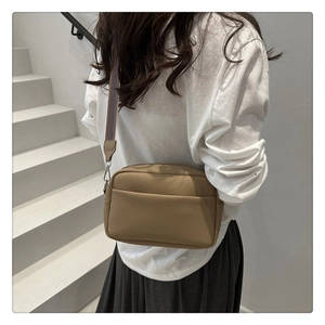 Detail of khaki litchi grain PU crossbody bag with stylish striped woven shoulder strap