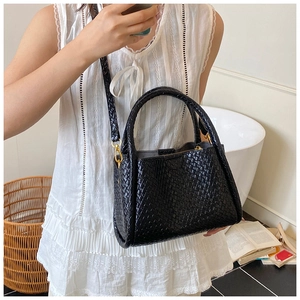 Détail d'un sac seau noir en cuir tressé avec finitions dorées porté par un mannequin