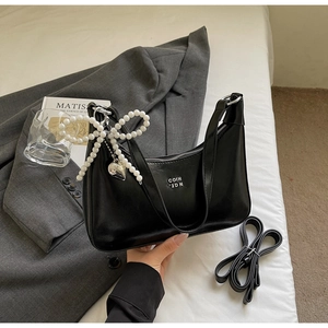 Detail of black PU leather dumpling bag featuring a pearl bow charm and heart pendant
