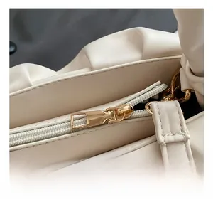 Detail of elegant gold-toned metal zipper hardware on a white pleated shoulder bag