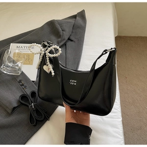 Detail of black dumpling bag featuring pearl bow charm and white letter print