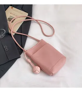 Close-up of pink litchi grain crossbody bag with woven ball knot and slim strap