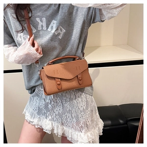 Detail of caramel textured leather crossbody bag with dual decorative buckles and strap