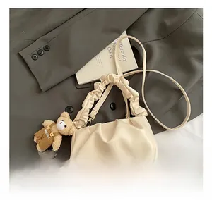 Detail of cream pleated cloud bag with stylish teddy bear charm on grey background