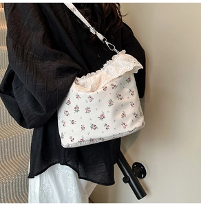 Floral shoulder bag with lace trim and adjustable strap shown on model over white skirt