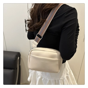 Rear view of a beige lychee pattern PU leather crossbody bag with a wide striped strap