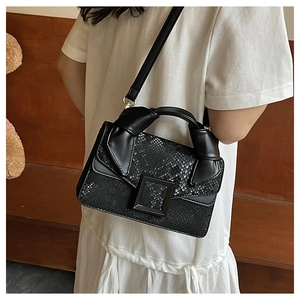 Detail of black snakeskin embossed crossbody bag with matte square buckle and knotted handle