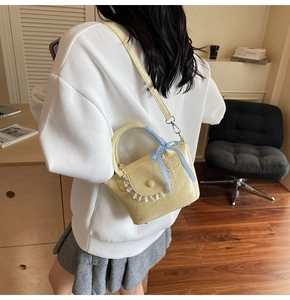 Detail view of yellow leather bucket bag featuring white lace trim and checkered bow accent
