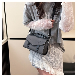 Detail of gray cross-grain leather crossbody bag with black handles and round decorative buckle