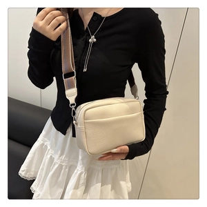 Close-up of cream crossbody camera bag with litchi texture and striped fabric strap