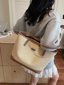 Large straw tote bag with brown leather trim and metal plaque shown on a shoulder