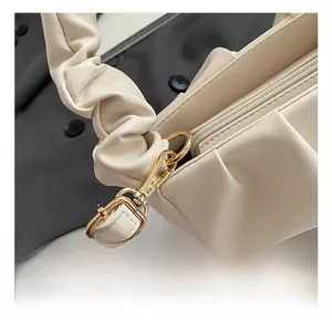 Detailed macro view of the golden metal hook and ruched shoulder strap of this beige bag