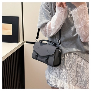 Detail view of a gray leather crossbody bag with silver buckles and a black round handle