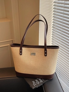 Straw and brown leather patchwork tote bag with metal plaque on a dark sofa