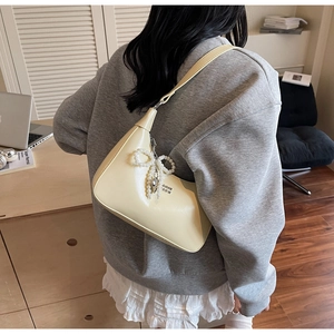 Detail of cream crescent bag with pearl bow pendant and metallic logo on PU leather