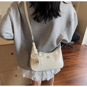 Close-up of beige faux leather hobo bag with pearl bow and silver heart pendant detail