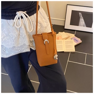 Detail of a brown leather bucket phone bag with silver horseshoe buckle and tassel charm
