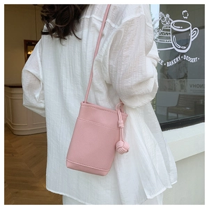 Pink mini crossbody phone bag with pebble leather texture and braided ball charm detail