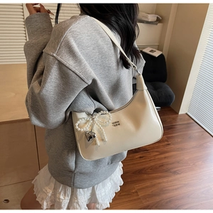 Detail of cream underarm bag with embossed letters, pearl bow, and heart charm