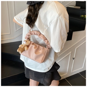 Detail view of pink pleated handbag with soft texture and cute teddy bear charm